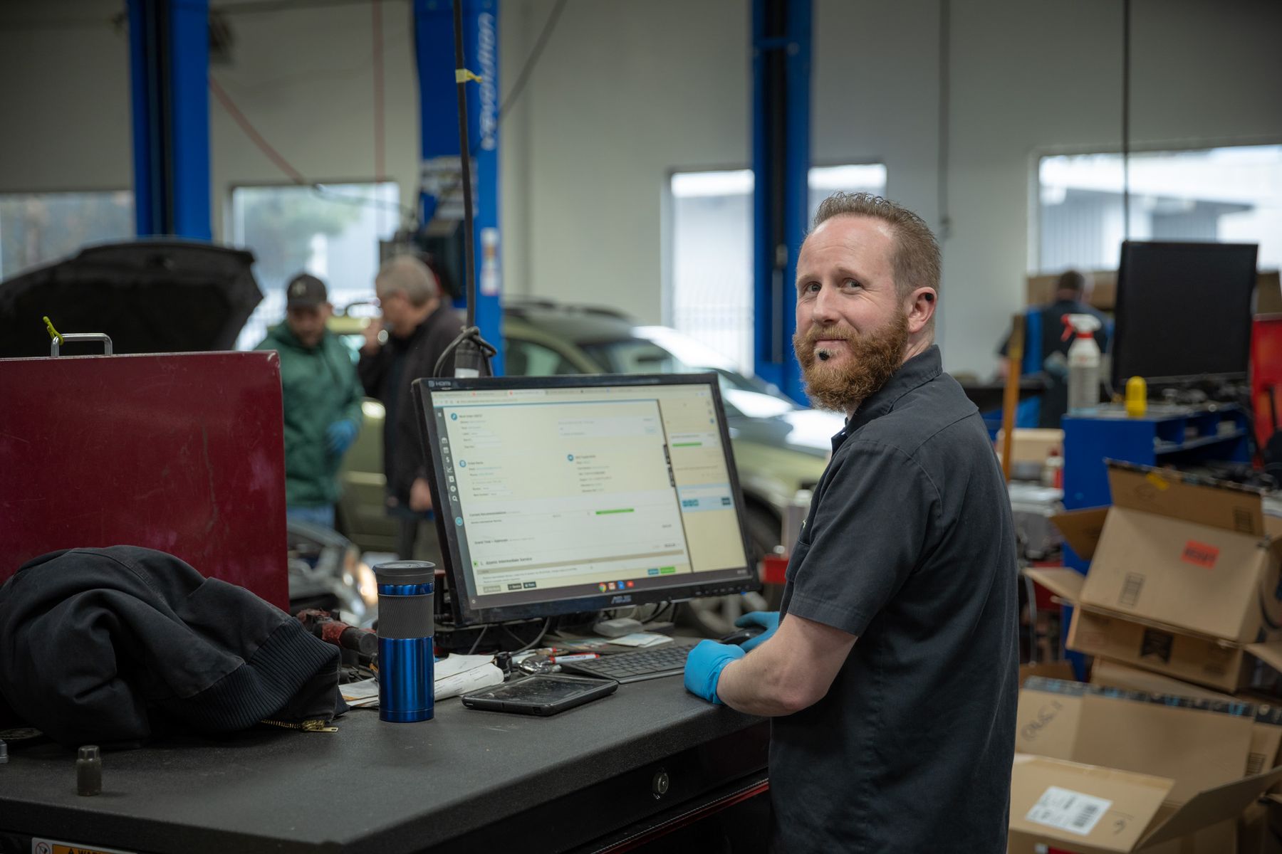 An Atomic technician in blue gloves at a diagnostic computer on the shop floor, looking back over his shoulder