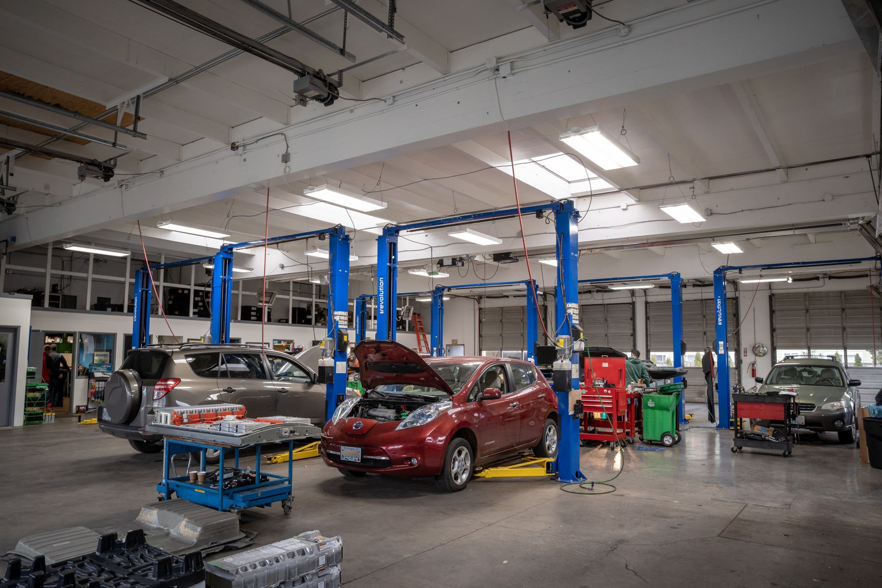 A Nissan Leaf with its hood up and a RAV4 on the lifts at Atomic Auto